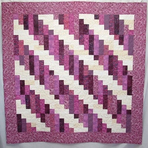 May include: A quilt with a geometric pattern of purple and white squares. The quilt is made with a variety of fabrics, including some with a floral pattern.