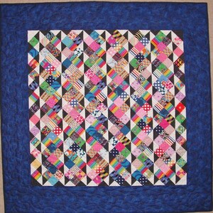 May include: A colorful quilt with a geometric pattern of black, white, and rainbow-colored triangles. The quilt is framed with a dark blue border.
