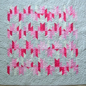 May include: A quilt with a geometric pattern of pink and white fabric squares on a gray background.