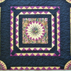 May include: A quilt with a black background and a multi-colored starburst design in the center. The starburst is surrounded by a series of borders in black, gold, and pink.