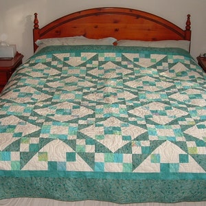 Puede incluir: Un edredón de color turquesa y blanco con un patrón geométrico está sobre una cama con una cabecera de madera y dos mesitas de noche con lámparas.