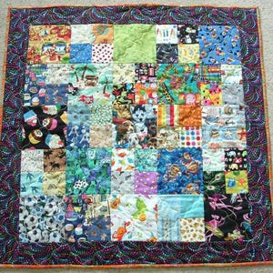 May include: A colourful patchwork quilt with a black and white border. The quilt is made up of many different squares of fabric, each with a different pattern. The quilt is perfect for a baby or child.