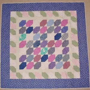 May include: A quilt with a geometric pattern of pink, purple, blue, and green squares. The quilt is surrounded by a blue border with a white floral pattern.
