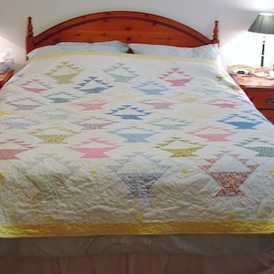 May include: A white bed with a yellow and white quilt featuring a basket pattern. The bed has a wooden headboard and a brown bed skirt. There are two nightstands with lamps on either side of the bed.