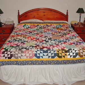 Könnte beinhalten: Ein Bett mit einer bunten Patchwork-Decke, einem weißen Bettrock und zwei Holz-Nachttischen mit Lampen.