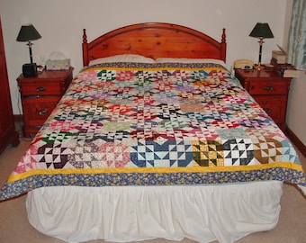 May include: A bed with a colorful patchwork quilt, a white bed skirt, and two wooden nightstands with lamps.