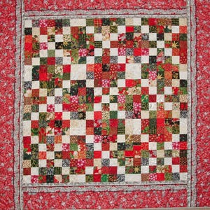 May include: A red, green and white patchwork quilt with a Christmas theme. The quilt is made up of small squares of fabric, each with a different pattern. The quilt is bordered with a red and white trim.