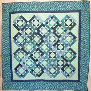 May include: A quilt with a geometric pattern in shades of blue and green. The quilt is made up of squares and triangles, and the pattern is repeated throughout the quilt.