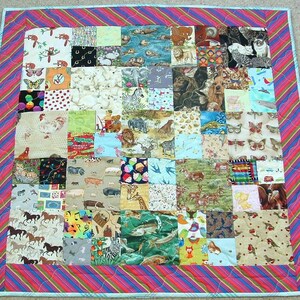 May include: A patchwork quilt featuring a variety of animal prints and patterns. The quilt is bordered with a striped fabric in shades of pink, blue, and red. The quilt is square-shaped and appears to be handmade.