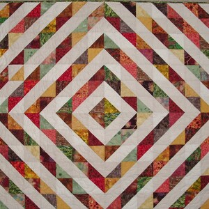 May include: A quilt with a geometric pattern of white, red, green, brown, and yellow triangles. The quilt is made of fabric with a variety of floral and abstract prints.