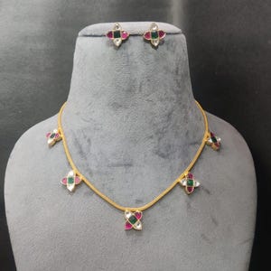 May include: A gold-colored necklace and matching earrings set. The jewelry features a floral design with red, green, and white gemstones. The necklace has multiple floral pendants, and the earrings have a single floral design.