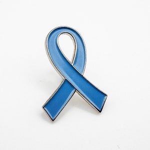 Könnte beinhalten: Eine blaue Schleifen-Anstecknadel, ein Symbol für Bewusstsein und Unterstützung.