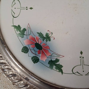 Op de afbeelding: Een wit keramiek bord met een zilveren rand en een bloemenmotief. Het ontwerp bevat roze bloemen, groene bladeren en blauwe accenten.