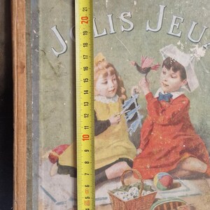 May include: Vintage children's book cover with the title "Mes Jolis Jeux." The cover features illustrations of two children playing with toys. The book measures approximately 10 inches tall. The publisher's name, HACHETTE, is printed at the bottom.