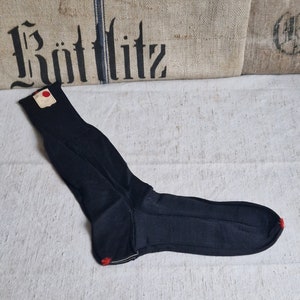 Könnte beinhalten: Eine schwarze Socke mit einem roten Etikett, das oben befestigt ist. Die Socke hat einen weißen Streifen oben und einen roten Streifen an der Ferse.