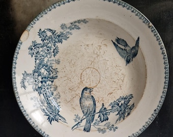 May include: Antique white ceramic plate with blue floral and bird illustrations. The plate features a detailed border design and a central bird perched on a branch. A vintage decorative piece.