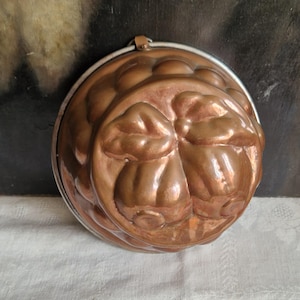 Könnte beinhalten: Eine Vintage-Kupferform mit einem dekorativen, abgerundeten Design. Die Form hat eine glänzende, metallische Oberfläche und einen silbernen Metallrand. Die Form wird wahrscheinlich zum Backen oder zur Herstellung dekorativer Lebensmittel verwendet.