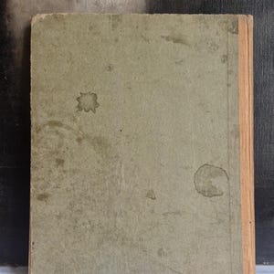 May include: A vintage book with a worn, light green cover. The cover has several dark stains and a faded appearance. The spine is a light tan color. The book appears to be old and well-used, with signs of age and wear.