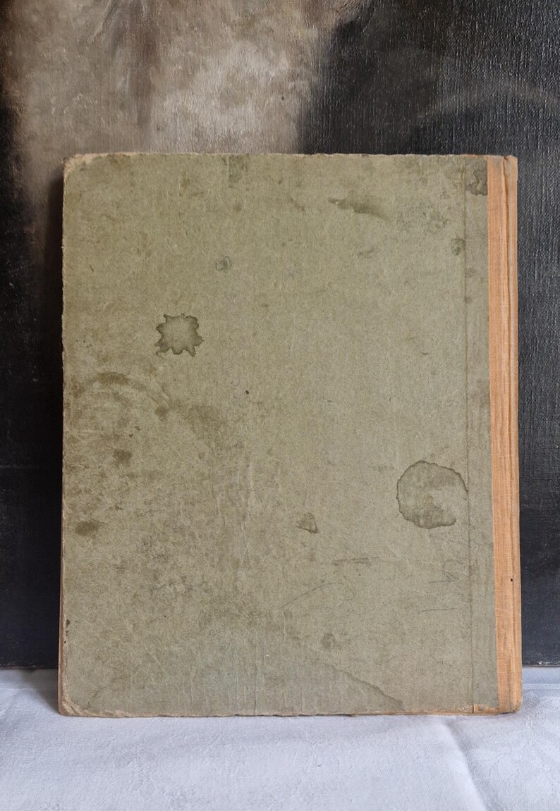 May include: A vintage book with a worn, light green cover. The cover has several dark stains and a faded appearance. The spine is a light tan color. The book appears to be old and well-used, with signs of age and wear.