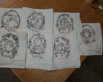 May include: Set of seven white tea towels with embroidered hedgehogs and floral designs. Each towel features a different day of the week, including Monday, Tuesday, Wednesday, Thursday, Friday, Saturday, and Sunday.