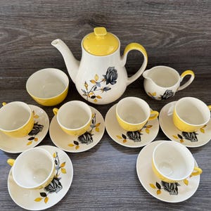 May include: A yellow and white tea set with a floral design. The set includes a teapot, creamer, sugar bowl, and six teacups and saucers.