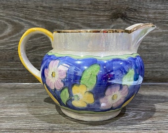 May include: A vintage cream and blue ceramic creamer with a gold rim and floral design. The flowers are pink, yellow, and green.