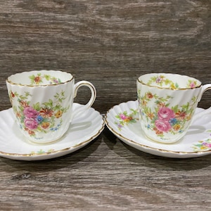May include: Two white teacups and saucers with a floral pattern. The cups have a gold rim and the saucers have a scalloped edge.