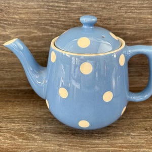 May include: A blue teapot with white polka dots. The teapot has a lid and a handle.