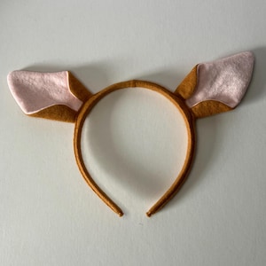 May include: A brown headband with two deer ears. The ears are made of brown and pink felt. The headband is a simple, circular design, perfect for costumes or themed events.