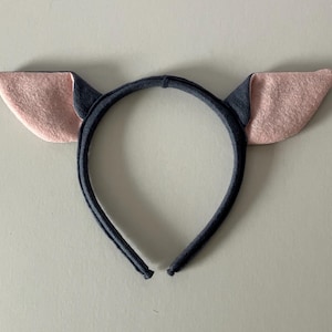 May include: A dark blue headband with two pink and dark blue felt ears. The ears are a light pink color on the inside and dark blue on the outside. The headband is made of a soft, flexible material.