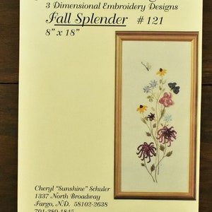 May include: A framed embroidery design titled "Fall Splender" by JDR Brazilian Elegance. The design features a bouquet of fall flowers in shades of purple, yellow, and white, with butterflies and a dragonfly. The design measures 8 inches by 18 inches.