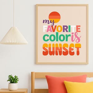 May include: A framed print with the text "my FAVORITE color is SUNSET" in colorful, retro-style lettering. The artwork features a stylized sunset graphic and is displayed above a bed with orange and yellow pillows.