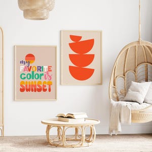 May include: Two framed art prints with a beige background. One print says "my favorite color is sunset" in colorful text. The other print has a design of orange semi-circles. A wicker hanging chair and round table are also in the image.