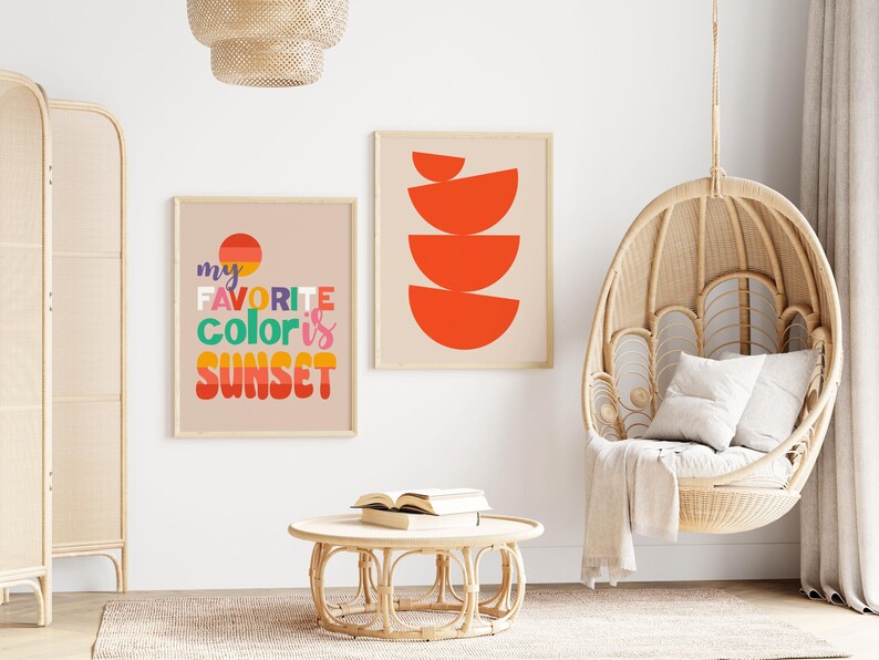 May include: Two framed art prints with a beige background. One print says "my favorite color is sunset" in colorful text. The other print has a design of orange semi-circles. A wicker hanging chair and round table are also in the image.