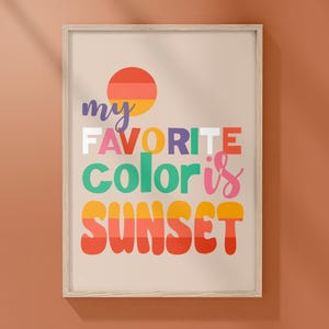 May include: A framed print with the text "my favorite color is SUNSET" in colorful, retro-style lettering. The design includes a stylized sunset graphic with orange, yellow, and red hues, set against a beige background.