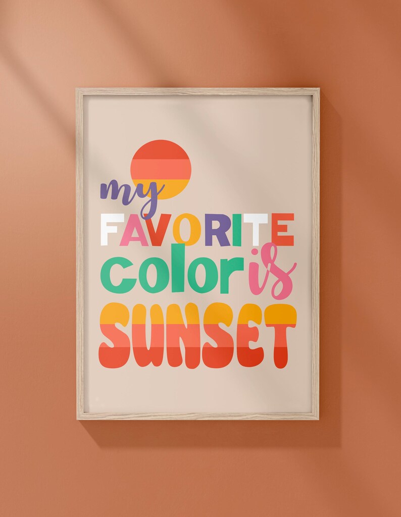 May include: A framed print with the text "my favorite color is SUNSET" in colorful, retro-style lettering. The design includes a stylized sunset graphic with orange, yellow, and red hues, set against a beige background.