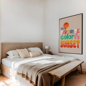May include: A bedroom scene featuring a bed with white linens, beige pillows, and a light brown blanket. A wooden bench sits at the foot of the bed. A framed poster on the wall reads "my favorite color is SUNSET" in colorful text.