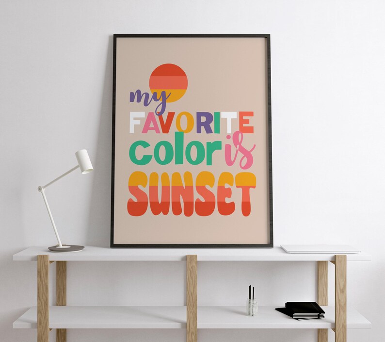 May include: A framed art print with the text "my FAVORITE color is SUNSET" in colorful, bold letters. The artwork features a stylized sunset graphic in shades of orange, yellow, and red, set against a neutral background. The print is displayed on a white shelf.
