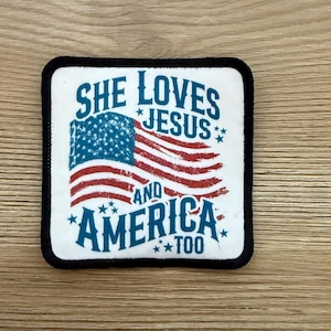 May include: Square patch with a white background and a black border. The patch features a stylized American flag in red, white, and blue. Text on the patch reads "SHE LOVES JESUS AND AMERICA TOO."