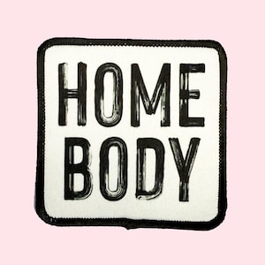 May include: Black and white iron-on patch with the text "HOME BODY" in a bold, handwritten font.
