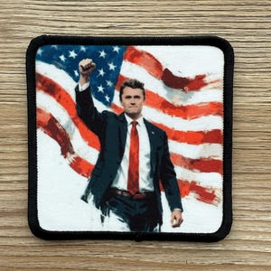 May include: A square patch with a black border features a man in a suit and red tie raising his fist in front of a painted American flag. The flag has red and white stripes and blue stars.