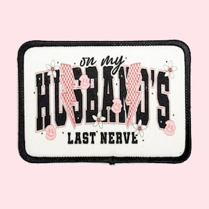 May include: White patch with black border featuring the text "on my husband's last nerve" in a black retro font with pink and white checkered lightning bolts and pink flowers.