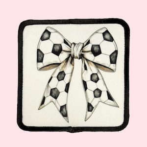 May include: A white fabric patch with a black border featuring a black and white soccer ball patterned bow.