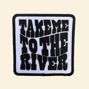May include: A white fabric patch with black text that reads "Take me to the river" in a retro font style.