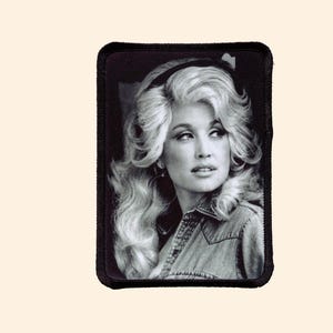 May include: Black and white photo of a woman with long blonde hair, wearing a denim jacket. She is looking off to the side and smiling slightly.