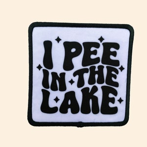 May include: White patch with black text that reads "I PEE IN THE LAKE" with a retro font and small black stars around the text.