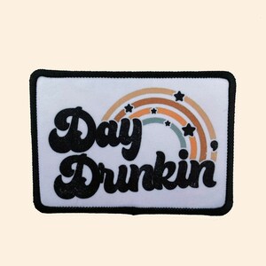 May include: White iron-on patch with black text that reads "Day Drinkin'" and a rainbow with stars in the colors brown, orange, yellow, green, and blue.