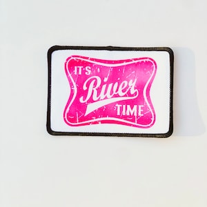 May include: Pink and white iron-on patch with the text "It's River Time" in a vintage style font.
