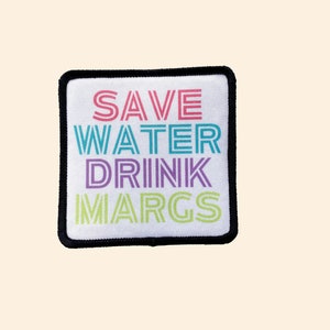 May include: A white square patch with black stitching around the edges. The patch has the text "SAVE WATER DRINK MARGS" in colorful, outlined letters.