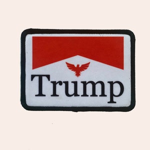 May include: A white and red patch with a black border. The patch features a stylized eagle with a red wingspan and the word "Trump" in black letters.